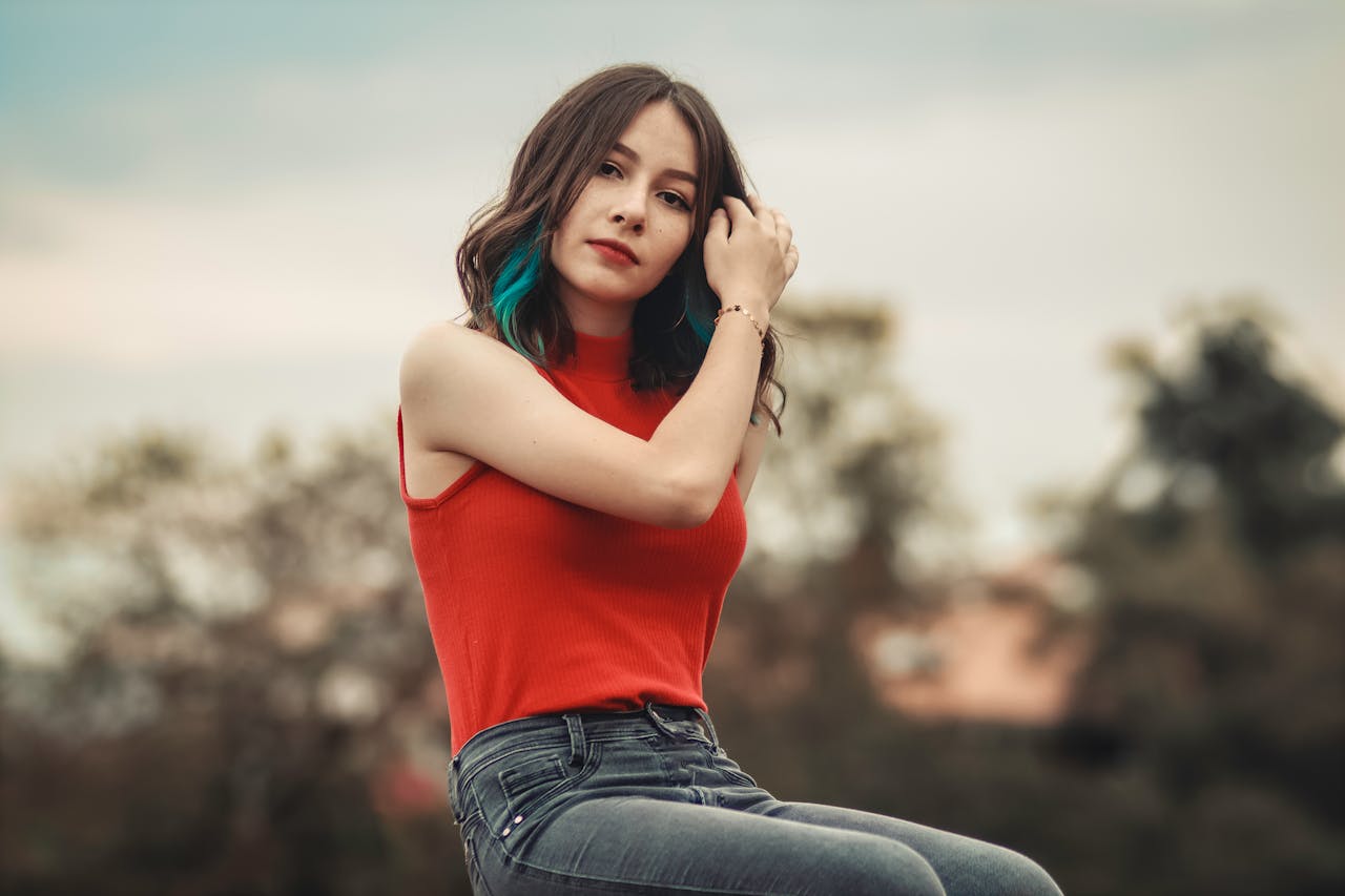 A fashionable young woman poses outdoors with a scenic background.